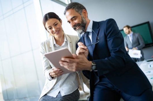 Happy business colleagues in modern office talking and using tablet